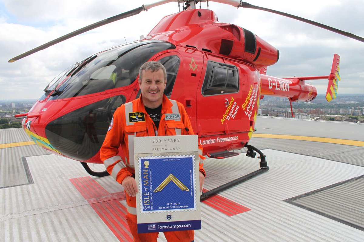 Pictured here is Manxman and Medical Director of London’s Air Ambulance, Dr Gareth Davies, on the landing pad at the Royal London Hospital, after being presented with a blow-up of the stamp and a donation of £1500 from Barbican Lodge, which is featured on one of the stamps.